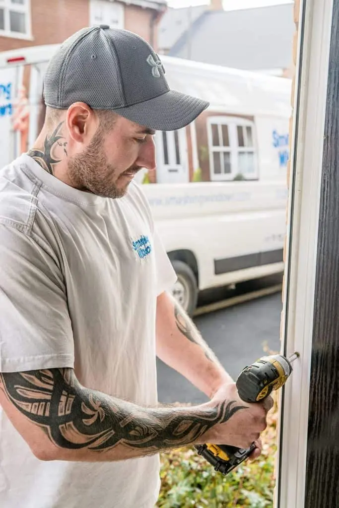 A Smashing Windows fitter using a cordless drill on a door frame, with the company van behind him