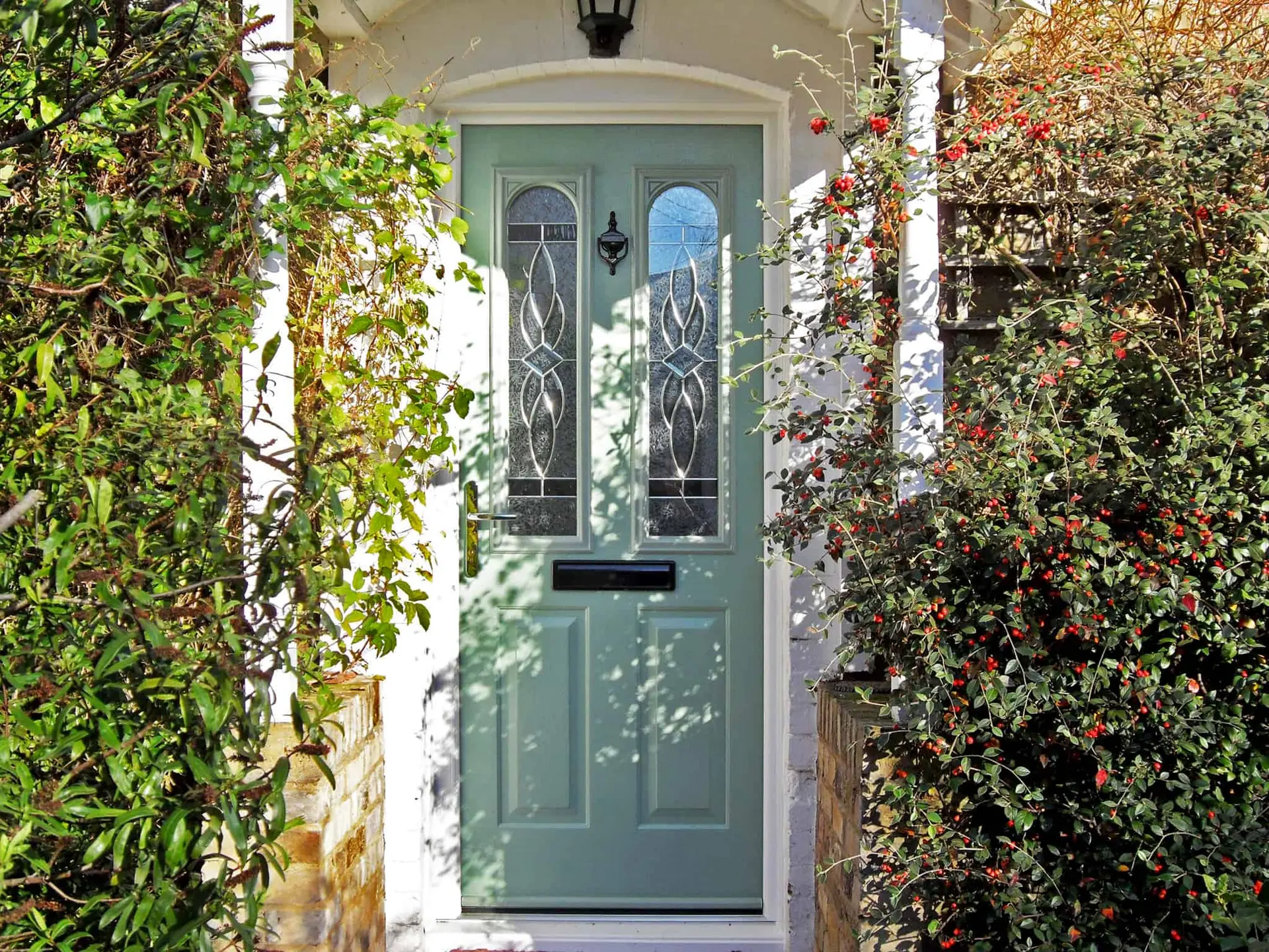 A sage green composite door with decorative glass panels, framed by climbing plants